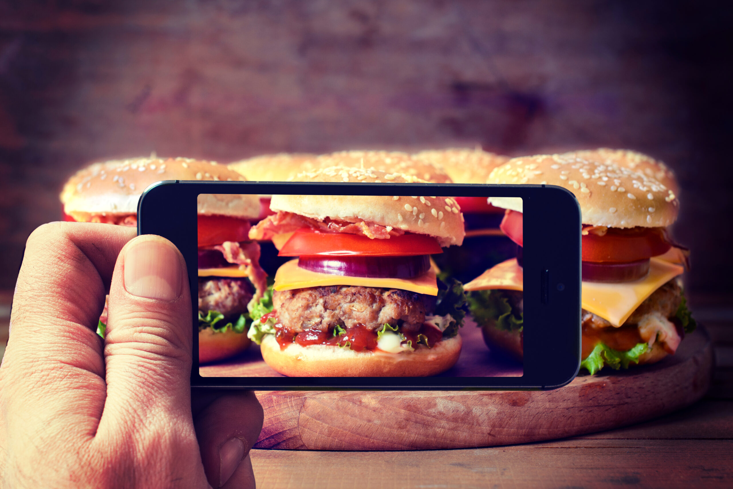 Man shooting with his cell phone camera big and tasty burgers.Selective focus on the phone